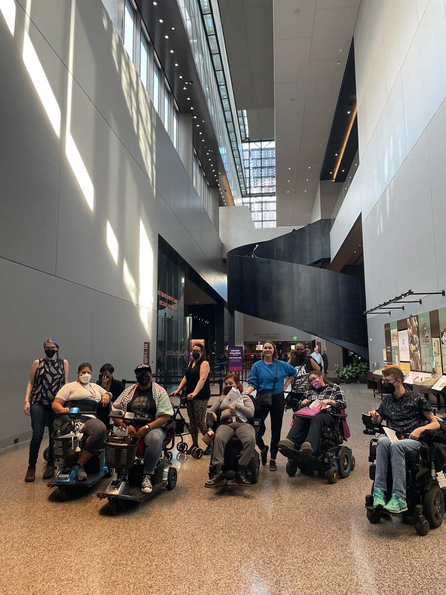 A group of US Alliance members, many using wheelchairs and scooters, gather inside the National Museum of African American History and Culture during the US Alliance in-person convening in Washington, DC.